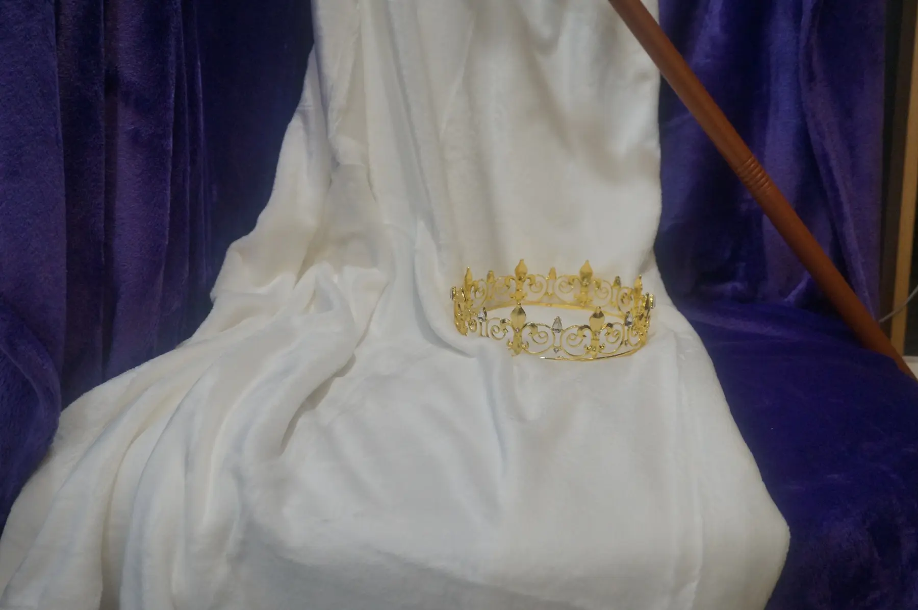 A gold crown resting at the foot of a white-draped throne