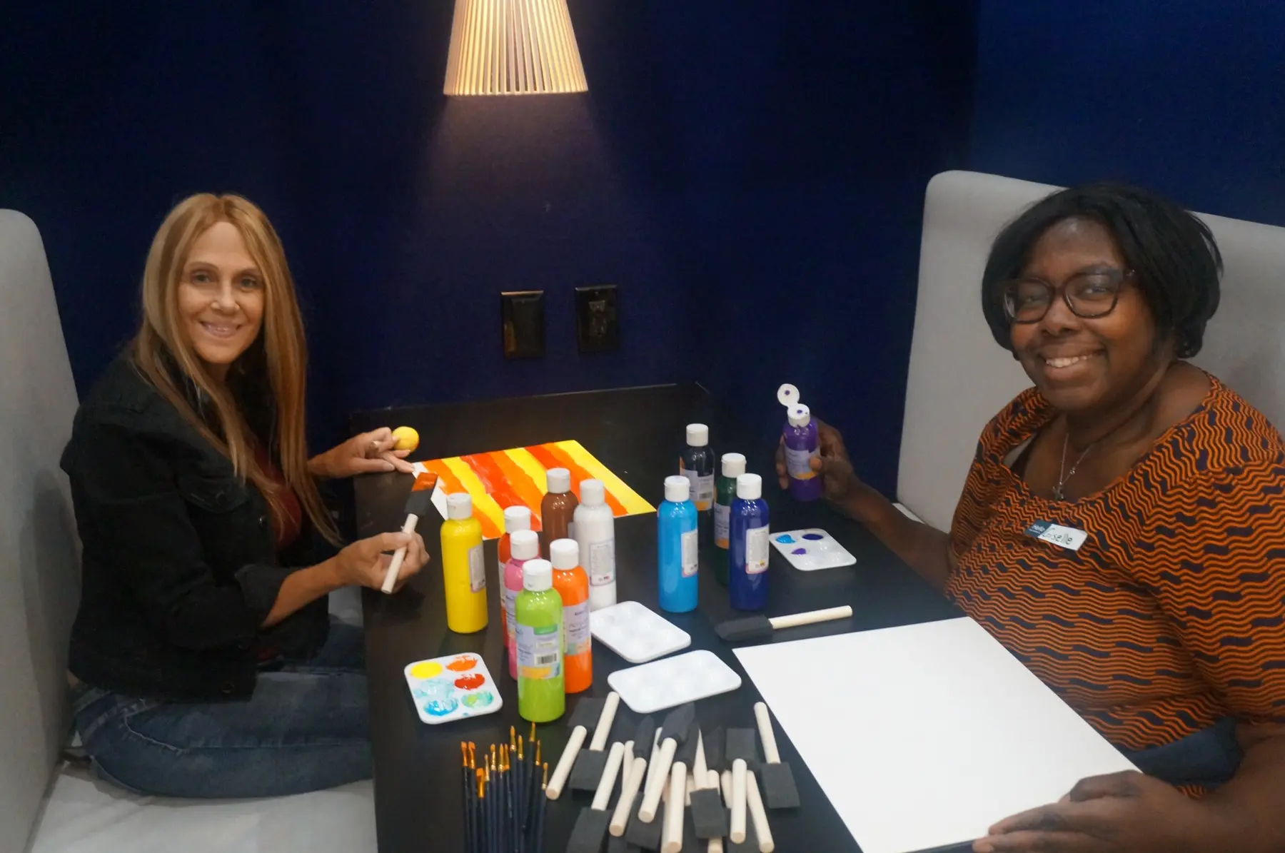 Two women smiling beside paint and blank boards